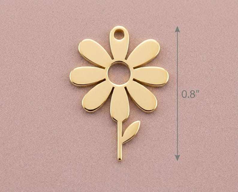 May include: A gold-coloured daisy charm with a stem and leaf, measuring 2 cm in height. The charm has a hole at the top for stringing. The daisy has six petals and a circular centre.