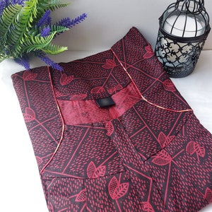 May include: A red and black patterned nightgown with a scoop neck and a gold trim. The nightgown is folded and laid flat on a white surface.