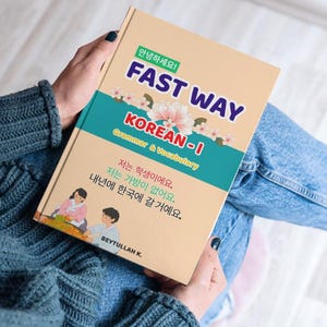 Puede incluir: Un libro de tapa dura titulado FAST WAY KOREAN-I Grammar & Vocabulary con una cubierta beige, una banda horizontal verde azulado e ilustraciones florales. La portada presenta texto en coreano, una ilustración de dos personas y el nombre BEYTULLAH K.