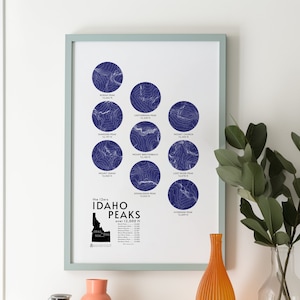 May include: A framed print of a map of Idaho with the 12 highest peaks over 12,000 feet. The peaks are represented by blue topographic circles with the name and elevation of each peak.