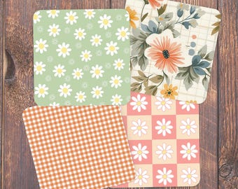 May include: Four square coasters with different patterns. One has a green background with white daisies, another has an orange gingham pattern, a third has a floral design, and the last has a pink and white checkerboard daisy pattern.