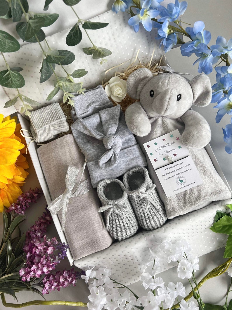 May include: A gray and white baby gift box with a gray elephant plush toy, a gray knitted hat, a gray knitted onesie, a gray knitted blanket, a pair of gray knitted booties, and a card that says "A Little Wish For Mummy".