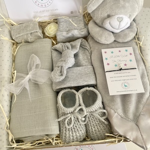 May include: A gray and white baby gift box with a gray knitted hat, booties, socks, a plush gray teddy bear, a gray blanket, and a white card with the text "A Little Wish For Mummy".