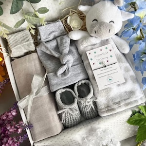 May include: A gray and white baby gift set in a white box with a white stuffed giraffe toy, a gray knitted hat, a gray knitted blanket, a gray knitted pair of booties, and a gray knitted sock. The box is decorated with white polka dots and the text "A Little Wish For Mummy".