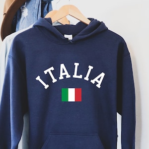 Puede incluir: Una sudadera con capucha azul marino con la palabra "ITALIA" en letras blancas y la bandera italiana impresa debajo.