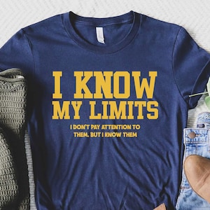 May include: A navy blue t-shirt with the text "I KNOW MY LIMITS I DON'T PAY ATTENTION TO THEM, BUT I KNOW THEM" in yellow lettering.
