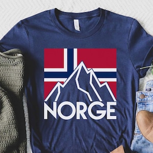 May include: A navy blue t-shirt featuring a white mountain graphic and the word "NORGE" printed on it. The mountain graphic is superimposed on a red, white and blue Norwegian flag.