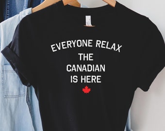 Pode incluir: Camiseta preta com texto branco que diz "Everyone Relax The Canadian Is Here" com uma folha de bordo vermelha abaixo do texto.