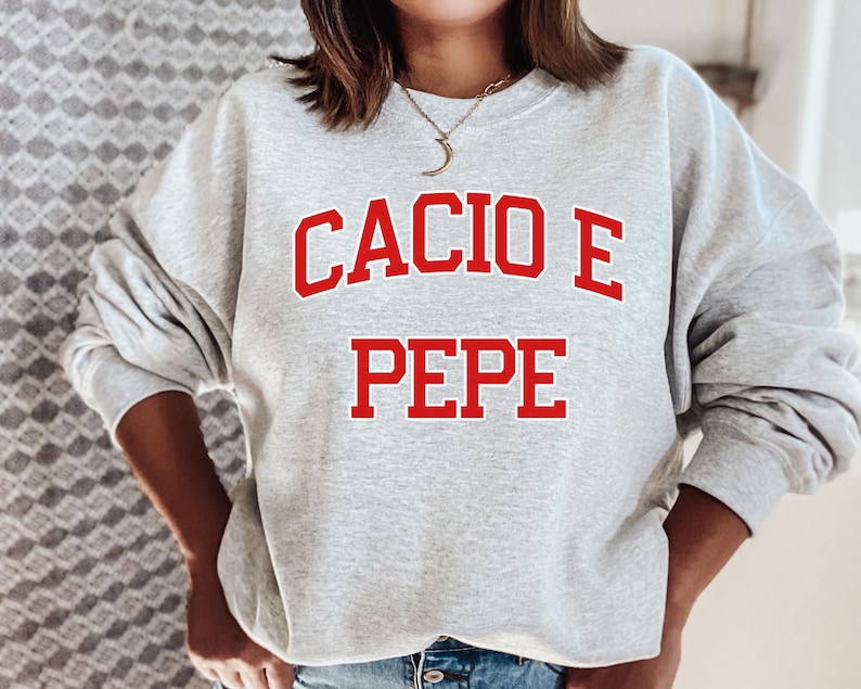 Puede incluir: Una sudadera gris con el texto "Cacio e Pepe" en rojo.
