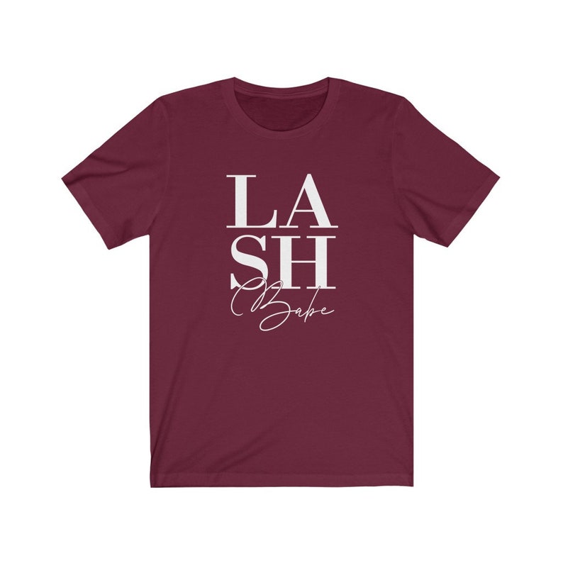 Pu&ograve; includere: T-shirt bordeaux a maniche corte con la scritta bianca &laquo;LASH Babe&raquo;. La parola &laquo;LASH&raquo; &egrave; impilata sopra &laquo;Babe&raquo;, con &laquo;SH&raquo; in mezzo. La parola &laquo;Babe&raquo; &egrave; in corsivo.