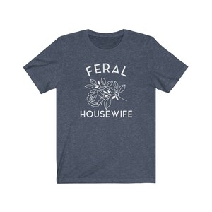 May include: A dark blue t-shirt with the text "FERAL HOUSEWIFE" in white lettering. A white outline of a rose with leaves is above the text.