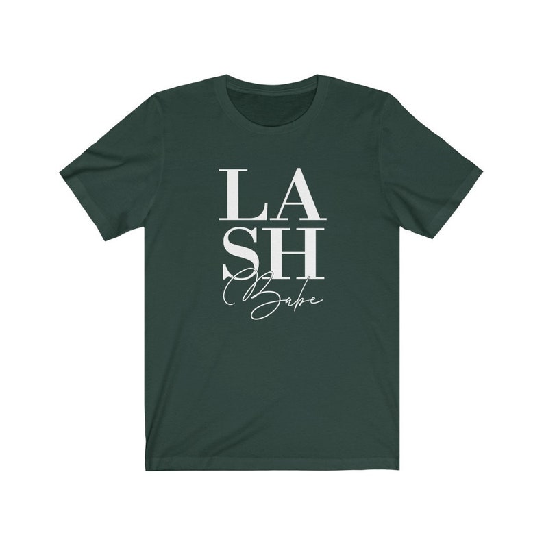Pu&ograve; includere: T-shirt verde scuro con la scritta bianca "LASH Babe". La parola "LASH" &egrave; sovrapposta a "Babe", con "SH" in mezzo. La parola "Babe" &egrave; in corsivo.