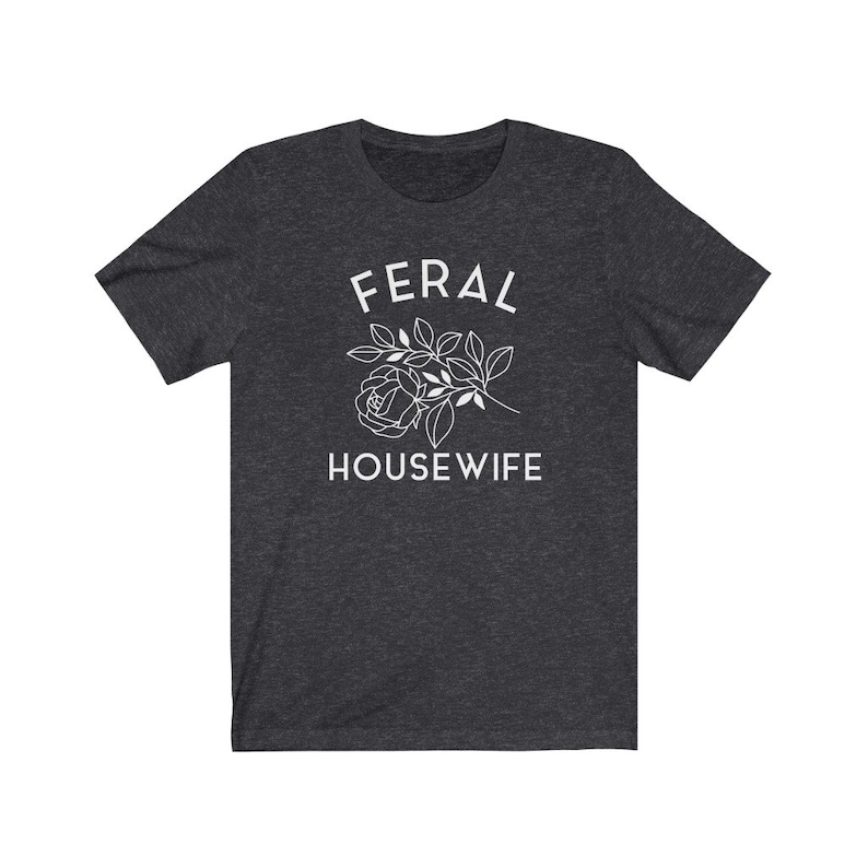 May include: A dark heather grey t-shirt with the text "FERAL HOUSEWIFE" in white lettering. A stylized white rose with leaves is above the text.