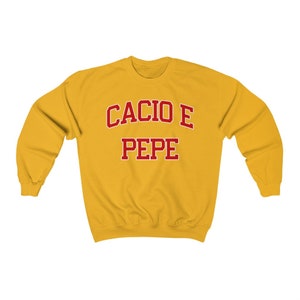 Puede incluir: Una sudadera amarilla con el texto "Cacio e Pepe" en rojo.