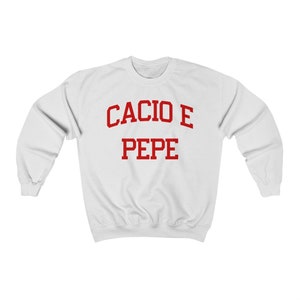 Puede incluir: Sudadera blanca con texto rojo que dice "Cacio e Pepe" en una fuente universitaria.