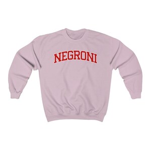 May include: A light pink sweatshirt with the word "NEGRONI" printed in red on the front.