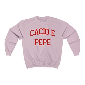 Puede incluir: Una sudadera de color rosa claro con el texto "Cacio e Pepe" en rojo.