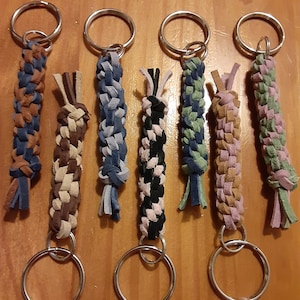 May include: Seven colorful braided leather keychains with silver key rings. The keychains are made of different colors of leather, including brown, blue, green, pink, and black.