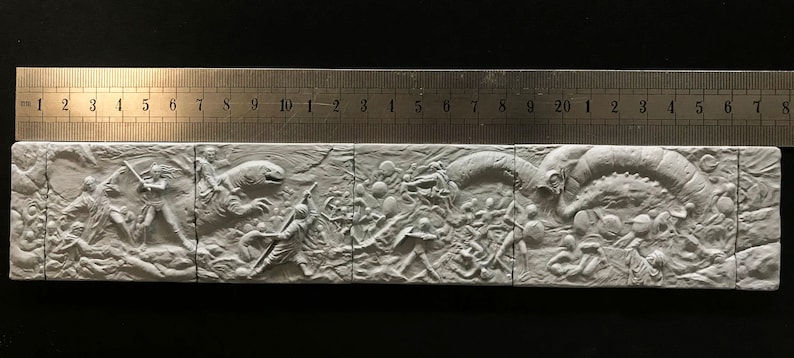 May include: A white, three-dimensional relief sculpture depicting a scene of a battle between humans and a large, serpentine creature. The sculpture is divided into four sections, each depicting a different part of the battle. The sculpture is made of plaster or a similar material.
