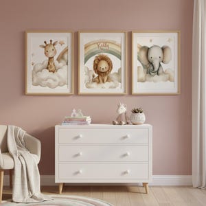 Peut inclure: Trois impressions encadrées à l'aquarelle représentant des animaux adorables. Une girafe, un lion avec le nom "Kelly" sur un arc-en-ciel et un éléphant sont représentés sur des nuages moelleux. Les impressions sont dans des cadres en bois clair, parfaits pour une chambre d'enfant.