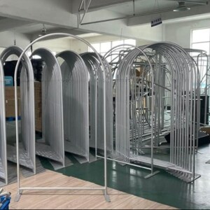 May include: A collection of silver metal archway frames, some assembled and some disassembled, in a warehouse setting.