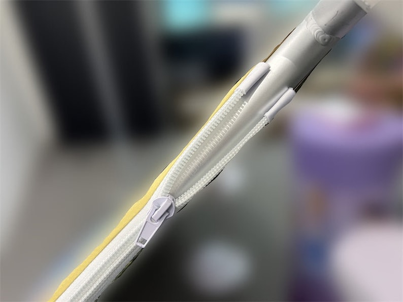May include: Close-up of a white zipper sewn onto a yellow fabric tube. The zipper is partially open, revealing the white fabric lining inside.
