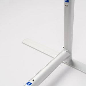 May include: Close-up of a silver metal display stand with a base and two adjustable poles. The poles have blue markings with the number "8" on them.