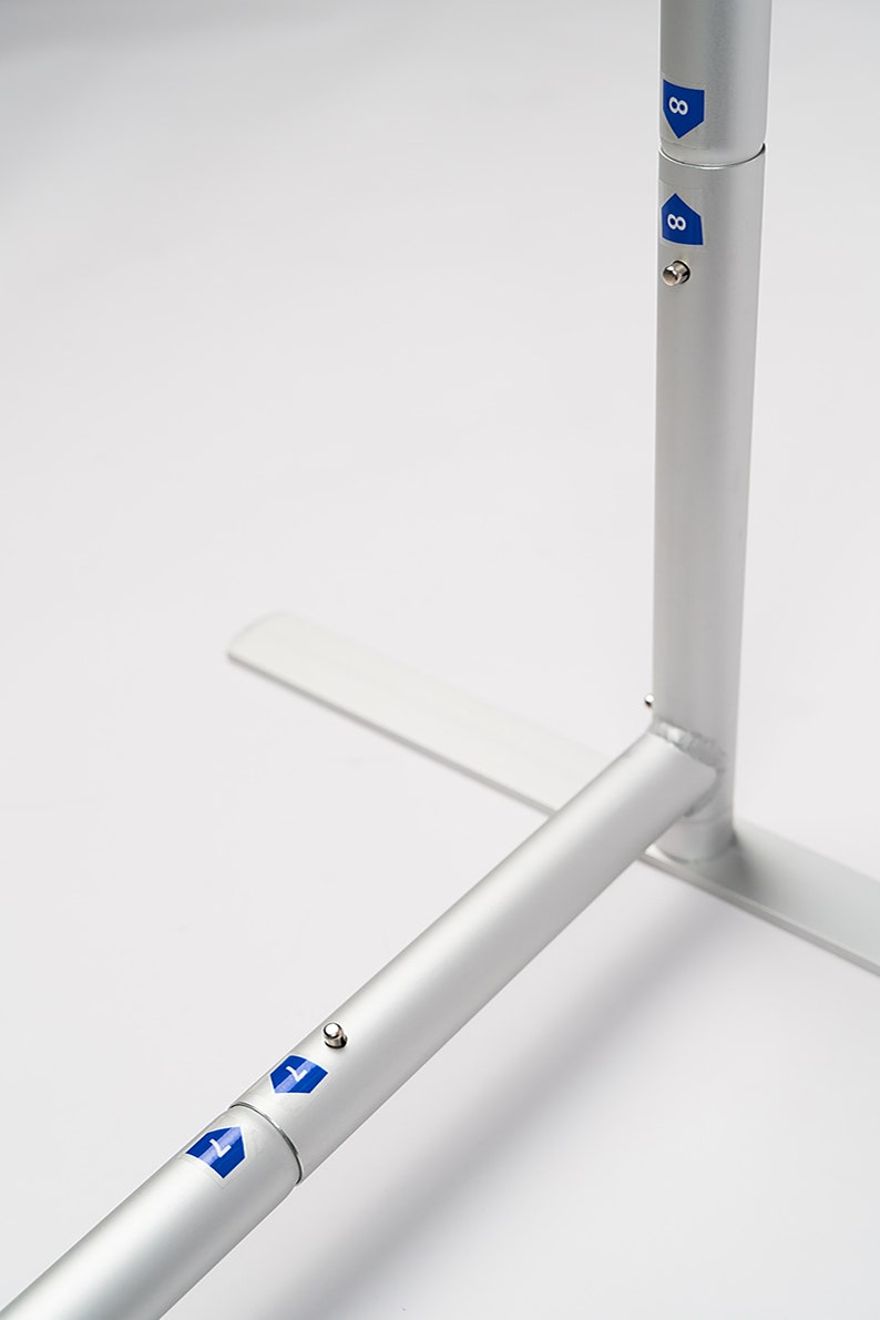 May include: Close-up of a silver metal display stand with a base and two adjustable poles. The poles have blue markings with the number "8" on them.