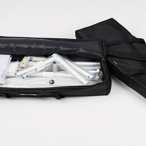 May include: Two black carrying cases with zippers and handles. One case is open and contains a white backdrop and silver poles.