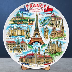 May include: A white decorative plate with illustrations of French landmarks, including the Eiffel Tower, and the cities of Paris, Nice, and Marseille. The plate is inscribed with the words "FRANCE" and "LIBERTÉ, ÉGALITÉ, FRATERNITÉ".