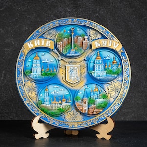 May include: A blue and gold ceramic plate with a decorative design featuring images of buildings and the text "КИЇВ KYIV".