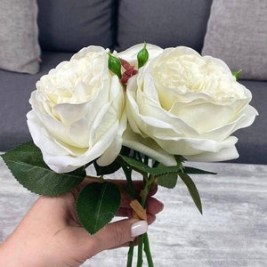 May include: A bouquet of white silk roses with green stems and leaves. The roses are arranged in a hand-tied bouquet.