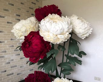 Könnte beinhalten: Ein Strauß großer Papier-Pfingstrosen in Weiß- und Rottönen. Die Blumen sind in einer Vase arrangiert und werden vor einer Backsteinwand ausgestellt.