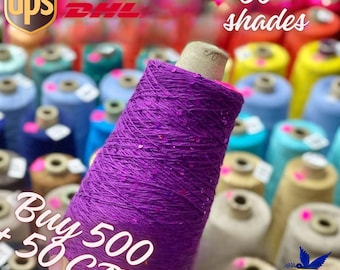 May include: A close-up of a spool of purple yarn with sequins. The yarn is surrounded by other spools of yarn in various colours. The text "Buy 500 + 50 Gift" is visible in the image.