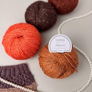 May include: A collection of colorful yarn balls in shades of orange, brown, and red, with a pearl necklace and a knitted swatch. The yarn balls have a speckled texture and a metallic sheen. The label on one ball reads "YARNA".
