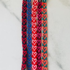 Puede incluir: Cinco pulseras de la amistad con un patrón de corazón. Las pulseras están hechas con hilo de bordar de colores en rojo, rosa, azul, negro y verde.