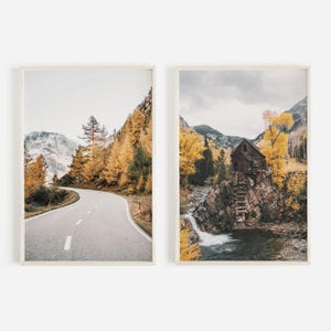 May include: Two framed landscape photographs. The first shows a winding road through a forest with yellow leaves in the fall. The second shows a wooden cabin with a waterfall in front of it, surrounded by trees with yellow leaves.