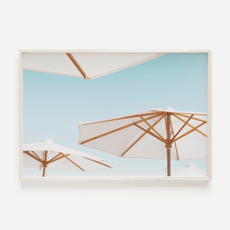 May include: Three white beach umbrellas with wooden frames against a light blue sky.