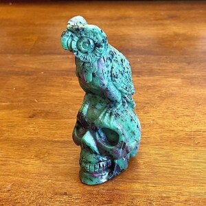 May include: A green and black carved jade skull with a green and black parrot perched on top of it.