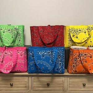 May include: Six rectangular quilted tote bags featuring a repeating paisley bandana pattern. The bags are available in bright lime green, red, yellow, hot pink, blue, and orange, each with two matching fabric handles and a structured rectangular shape.