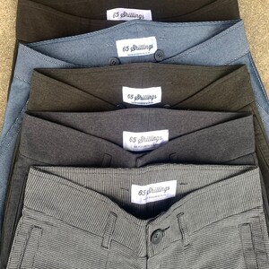 May include: Five pairs of grey, black and blue trousers with a white label that says "65 Shillings" on each pair.