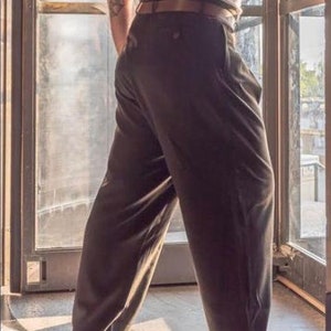 May include: A person wearing a pair of dark grey pleated trousers with a brown belt.