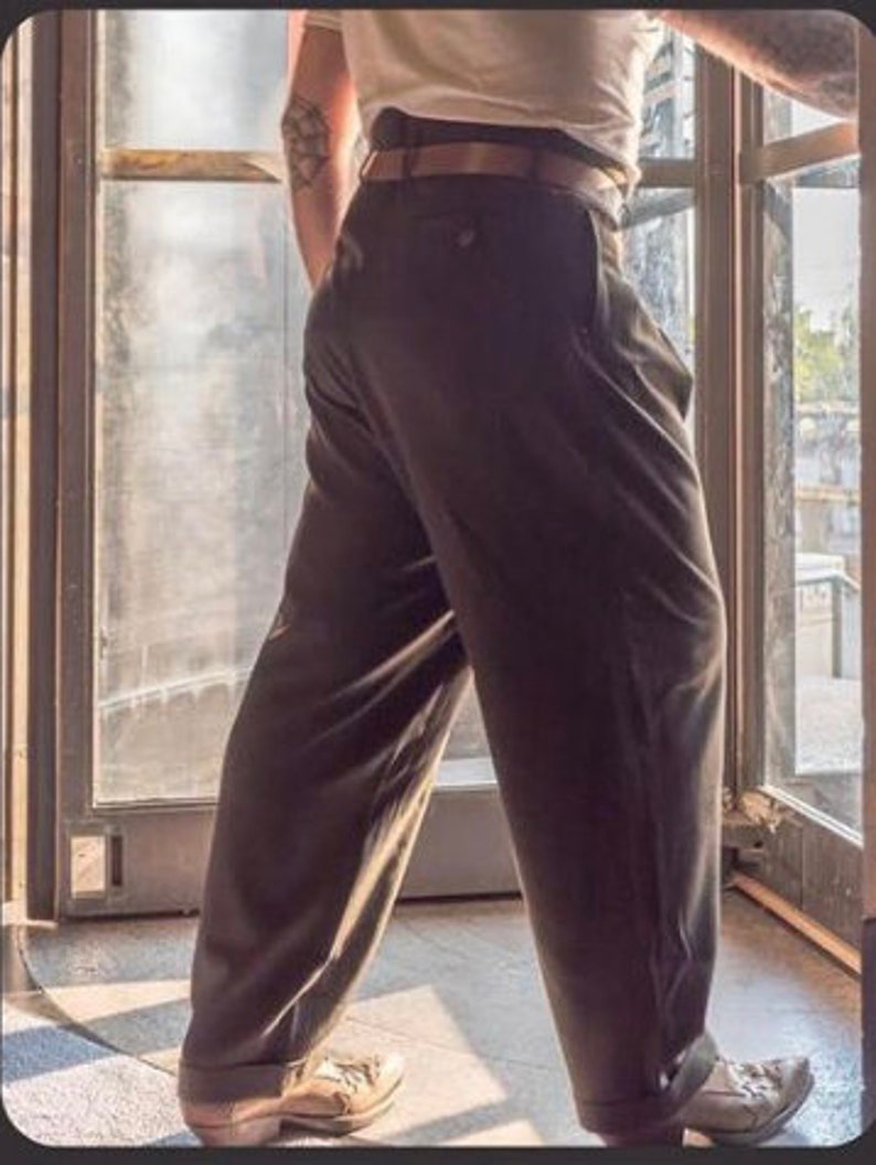 May include: A person wearing a pair of dark grey pleated trousers with a brown belt.
