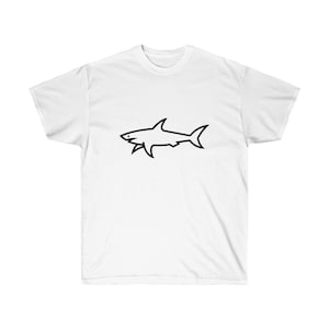 May include: White t-shirt featuring a black outline of a shark. The shark design is centered on the front of the shirt. The shirt has short sleeves and a crew neck.