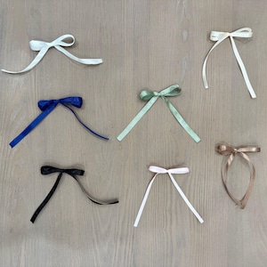 May include: Assortment of eight different coloured ribbon bows tied in a simple knot. The bows are arranged in two rows of four on a light wood surface.