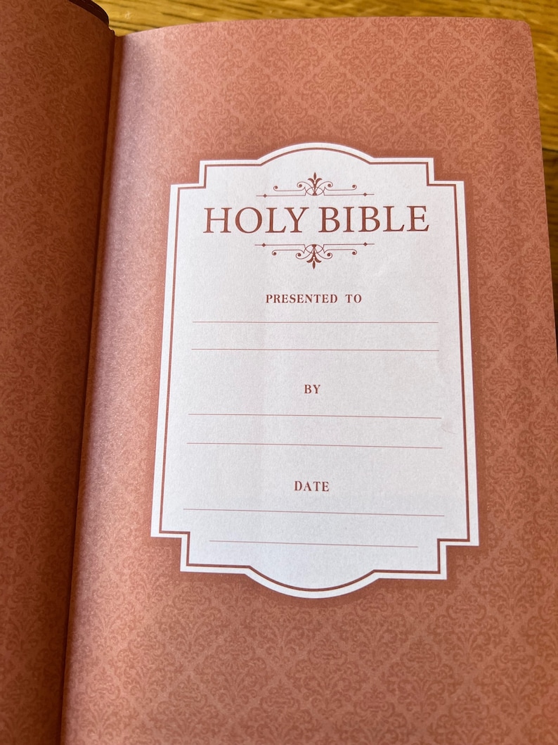 May include: Open Bible with a decorative, patterned cover in shades of peach and burgundy. The inside cover features a white label with the words "HOLY BIBLE" and spaces to write "PRESENTED TO", "BY", and "DATE".