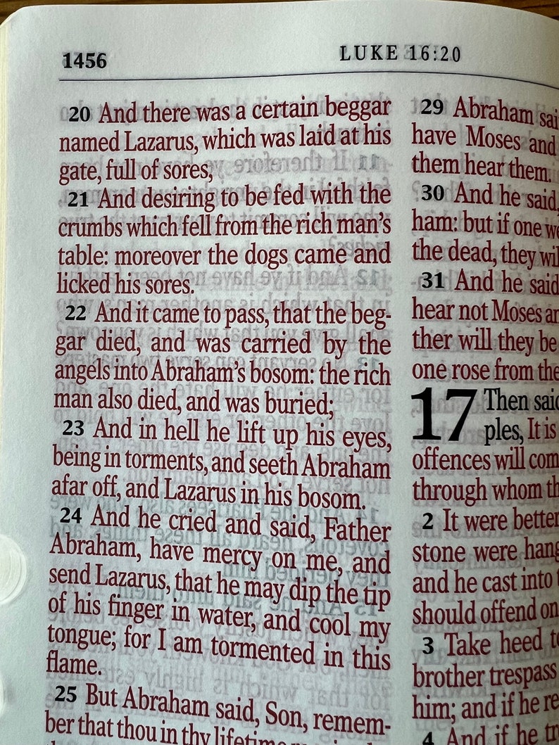 May include: Open Bible pages with text from Luke 16:20-25, in a close-up shot. The text is in a dark red font, with the chapter and verse numbers in bold. The paper is off-white, and the text is clear and easy to read.