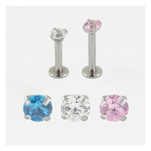 May include: Three pairs of surgical steel body jewelry with clear, blue, and pink gem stones. Each piece has a flat back and a post with a ball top.