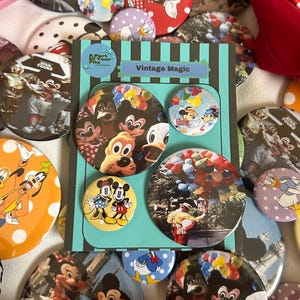 May include: A collection of vintage-style pinback buttons featuring various Disney characters. The buttons are round and colorful, with images of Mickey Mouse, Minnie Mouse, Donald Duck, and Goofy. Some buttons have the text "Vintage Magic".