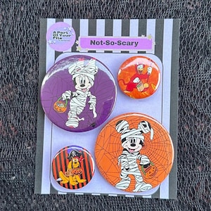 May include: A set of four circular pinback badges on a striped display card labelled Not-So-Scary. The badges feature cartoon characters dressed in Halloween costumes, including a mummy mouse, a devil duck, and a pirate dog with candy buckets.